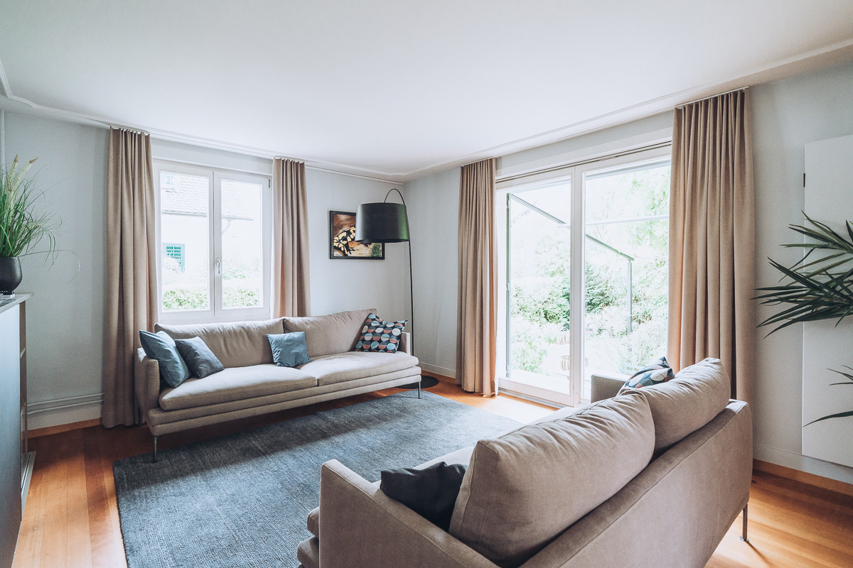 Ansicht einer Wohnungseinrichtung mit Holzm&ouml;beln, gepolstertem Sofa und Vorh&auml;ngen